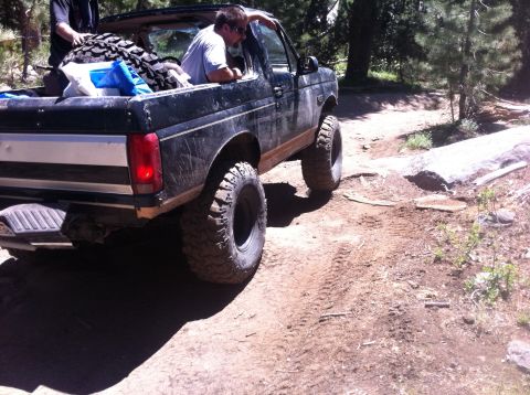 1990 Ford Bronco - This black SUV navigates a rough dirt path, equipped with off-road tires for challenging terrain.