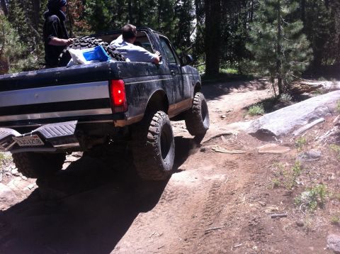 1990 Ford Bronco - 1990 Ford Bronco navigates a rocky off-road trail in a wooded area.