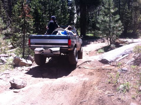 1990 Ford Bronco - A Ford F-Series pickup navigates a rocky trail through a forest with passengers in the truck bed.
