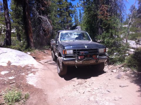 1990 Ford Bronco - This 1990 Ford Bronco is shown off-roading on a , rocky path surrounded by trees and boulders.