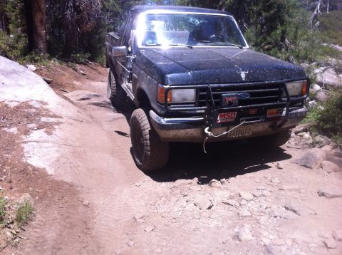 1990 Ford Bronco - Ford Bronco navigates a challenging rocky trail in a wooded area.