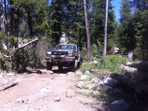 1990 Ford Bronco - This 1990 Ford Bronco is shown tackling a challenging off-road path surrounded by trees.