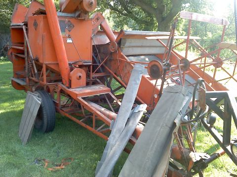 2000 Chevrolet Tahoe - An old orange combine harvester sits on a grassy field, showing signs of age and disuse.