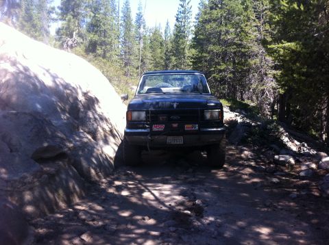 1990 Ford Bronco - This 1990 Ford Bronco is shown navigating a challenging rocky trail surrounded by trees.