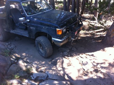 1990 Ford Bronco - This 1990 Ford Bronco is shown tackling a challenging off-road course with large rocks and trees.