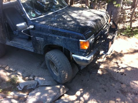 1990 Ford Bronco - This Ford Bronco is navigating a challenging, rocky trail with its driver's door ajar.