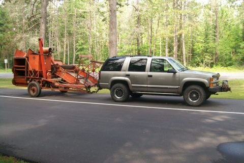 2000 Chevrolet Tahoe - A silver Chevrolet Tahoe tows a large orange agricultural machine on a road bordered by trees.