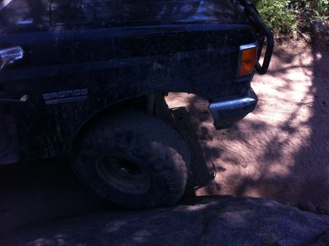 1990 Ford Bronco - A black Ford Bronco navigates a rocky, off-road trail with its front wheel on a large rock.