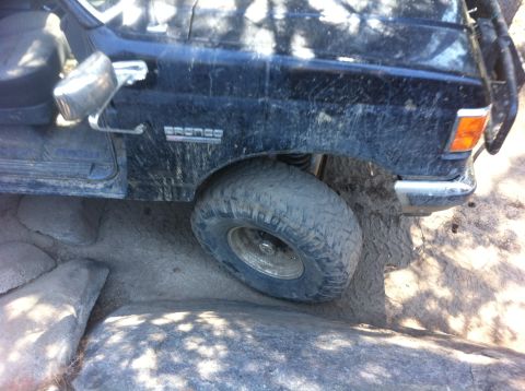 1990 Ford Bronco - This black 1990 Ford Bronco navigates rocky terrain, showing its front fender and tire.