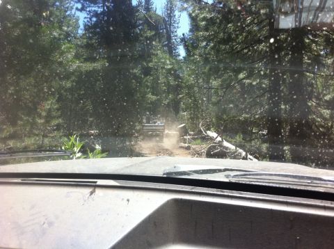 1990 Ford Bronco - Another vehicle kicks up dust on a rough forest road, seen from inside a car.