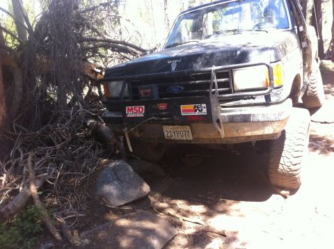 1990 Ford Bronco - A black Ford Bronco navigates challenging rocky terrain, its front end partially obscured by debris.