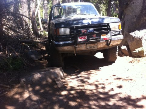 1990 Ford Bronco - This Ford Bronco is navigating a rough, off-road path with large rocks and trees.