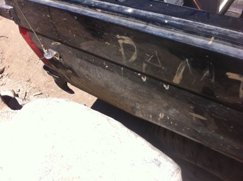 1990 Ford Bronco - Writing is scratched into the dirty rear quarter panel of a black vehicle.