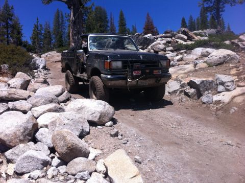 1990 Ford Bronco - Ford F-Series pickup truck driving on a rocky trail in a mountainous area.