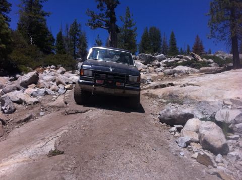 1990 Ford Bronco - A Ford Bronco navigates a challenging rocky terrain under a clear blue sky.