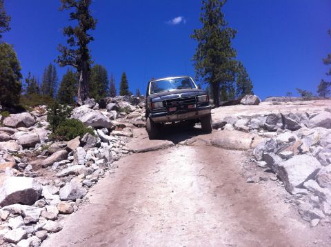 1990 Ford Bronco - Ford Bronco tackling a challenging rocky trail under a clear blue sky.