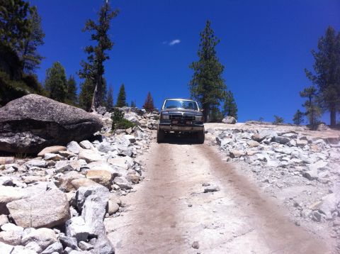 1990 Ford Bronco - A dark gray Ford Bronco navigates a challenging rocky terrain under a clear blue sky.