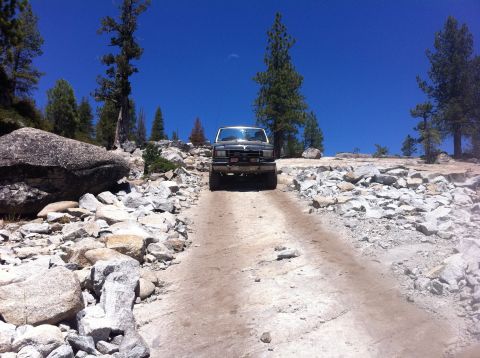 1990 Ford Bronco - A 1990 Ford Bronco navigates a challenging rocky terrain under a clear blue sky.