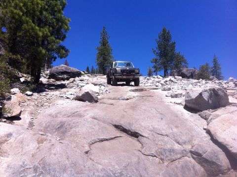 1990 Ford Bronco - A truck navigates a challenging off-road path under a clear blue sky.