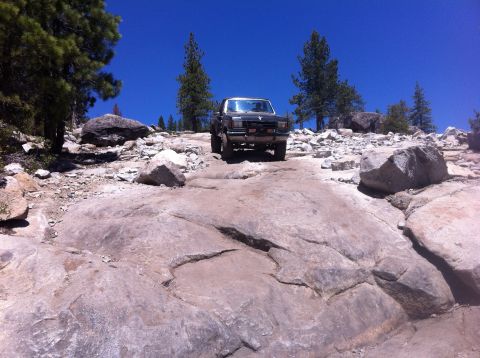 1990 Ford Bronco - A dark gray Ford Bronco navigates a challenging rocky terrain under a clear blue sky.
