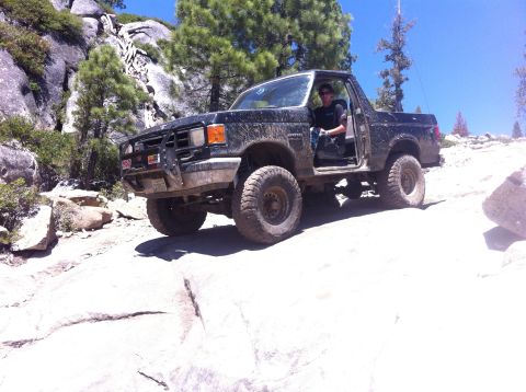 1990 Ford Bronco - A black Ford Bronco navigates a challenging rocky terrain on a sunny day.