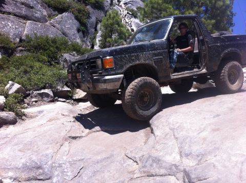 1990 Ford Bronco - A black Ford Bronco is driven over large rocks on a sunny day.