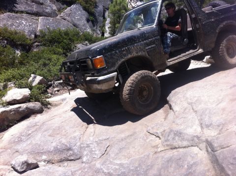 1990 Ford Bronco - This black off-road SUV navigates a challenging rocky trail, its lifted suspension and tires.