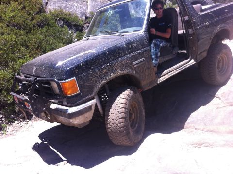 1990 Ford Bronco - A black Ford Bronco navigates a rocky trail with a driver inside.