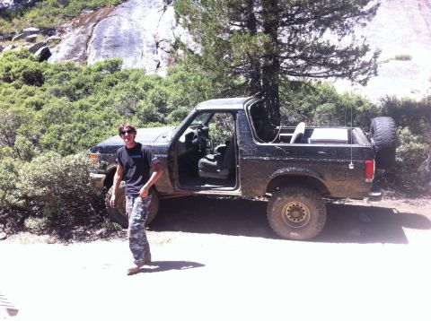 1990 Ford Bronco - A man poses with his off-road vehicle in a natural, rocky environment.