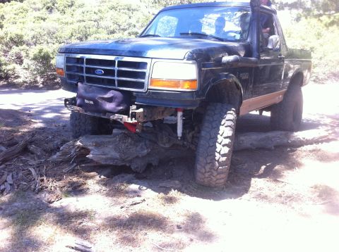 1990 Ford Bronco - This black Ford Bronco is navigating an obstacle course with large logs under its tires.