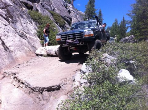 1990 Ford Bronco - A modified Ford Bronco navigates a challenging off-road trail with steep inclines and large rocks.