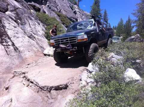 1990 Ford Bronco - A modified Ford Bronco navigates a challenging rocky off-road path with a second vehicle visible in the background.