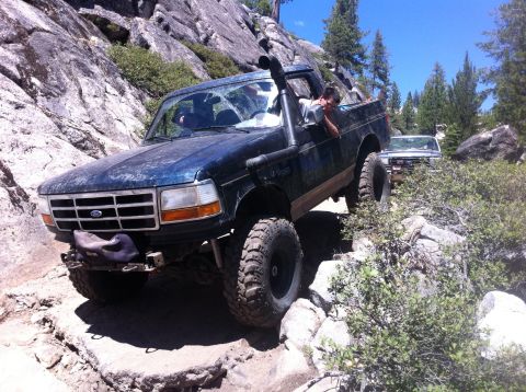 1990 Ford Bronco - A blue 1992 Ford Bronco navigates a rocky trail, equipped with a snorkel for off-road adventures.