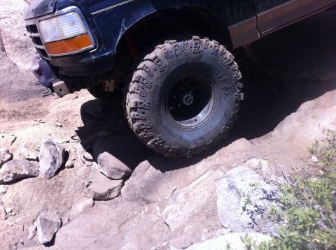 1990 Ford Bronco - This SUV is tackling a challenging rocky trail, with its front tire angled over a large boulder.