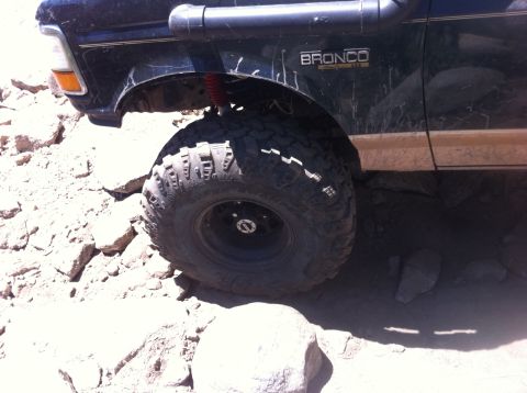 1990 Ford Bronco - A dark green Ford Bronco navigates rocky terrain, showing its off-road modifications.