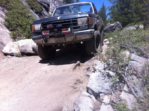 1990 Ford Bronco - A modified Ford Bronco navigates a challenging rocky trail in a mountainous area.