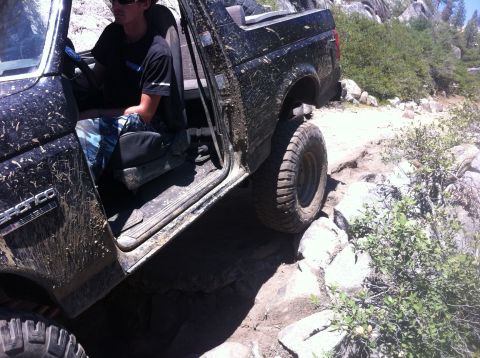 1990 Ford Bronco - A driver maneuvers a dirty Ford Bronco over a challenging, rocky off-road path.