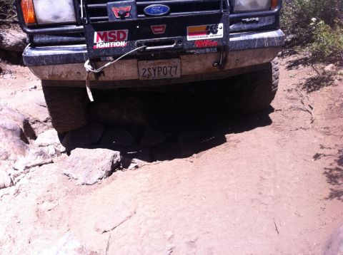 1990 Ford Bronco - Vehicle navigating a difficult rocky trail, showing its front bumper and tires.