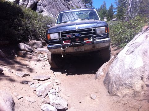 1990 Ford Bronco - A dark blue Ford Bronco navigates a challenging rocky off-road trail.