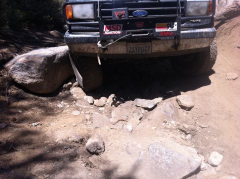 1990 Ford Bronco - A black Ford Bronco navigates a challenging rocky path, its front end visible.