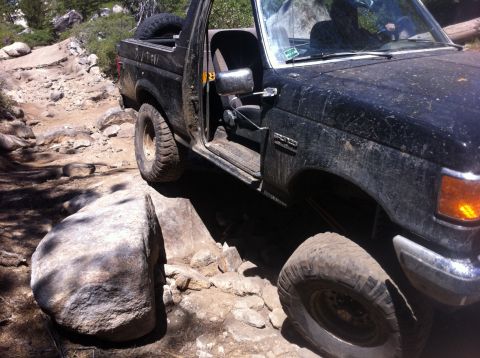 1990 Ford Bronco - This black 1990 Ford Bronco tackles a challenging rocky off-road path, with the driver visible behind the wheel.