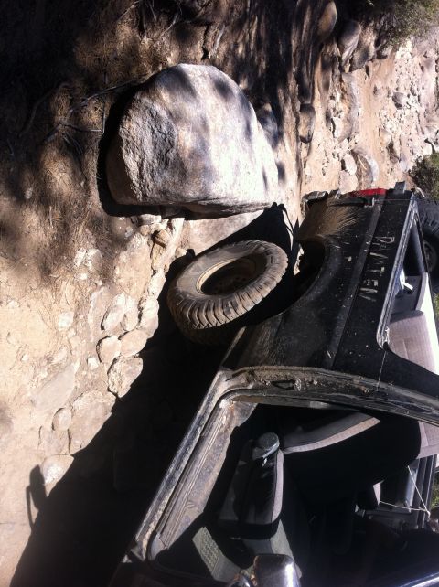 1990 Ford Bronco - SUV overturned on a rocky incline, with a large boulder resting against it.