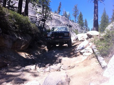 1990 Ford Bronco - A black Ford Bronco tackles a challenging rocky path on a sunny day.