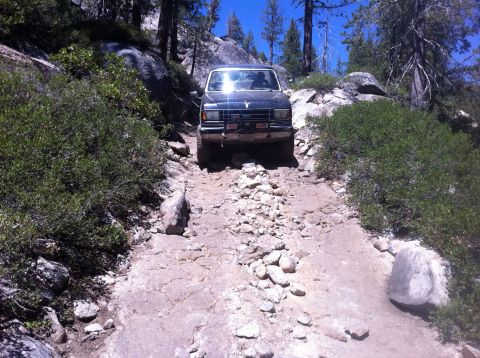 1990 Ford Bronco - A vehicle navigates a challenging, rocky path through a wooded, mountainous area.