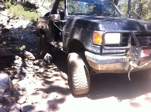 1990 Ford Bronco - This 1990 Ford Bronco navigates a challenging, rocky off-road path under a sunny sky.