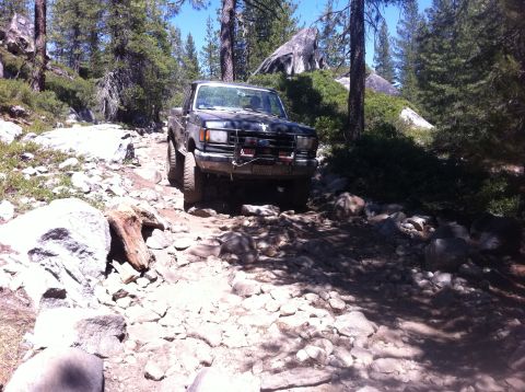 1990 Ford Bronco - This 1990 Ford Bronco tackles a challenging off-road path through a wooded, rocky landscape.