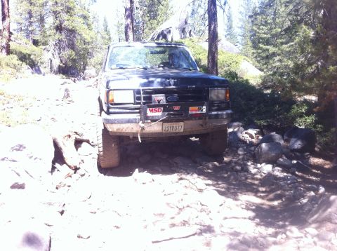 1990 Ford Bronco - Ford Bronco on a rough, off-road trail with trees and rocks.