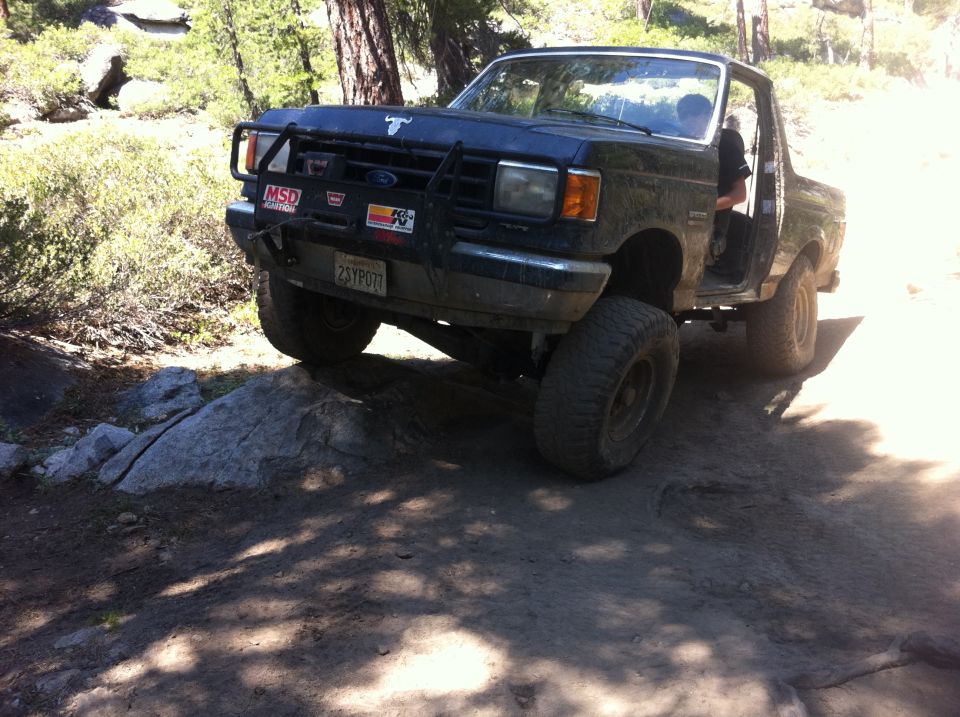 Ford Bronco off-roading on a dirt trail with large tires and a brush guard