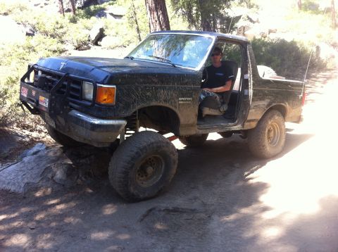 1990 Ford Bronco - A black, lifted Ford Bronco with a brush guard navigates a rocky, wooded trail.
