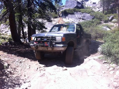 1990 Ford Bronco - A dark green Ford Bronco navigates a challenging, rocky off-road trail.